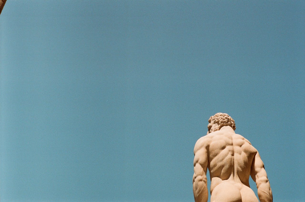 A classical marble statue from behind against a clear blue sky, showcasing artistic details.